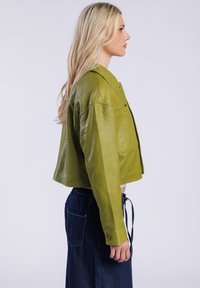 Przecinana skórzana kurtka w żywej zielonej kolorze, z klasycznym kołnierzykiem i kieszeniami z przodu. Nosi się ją na wysokim talii dżinsów.