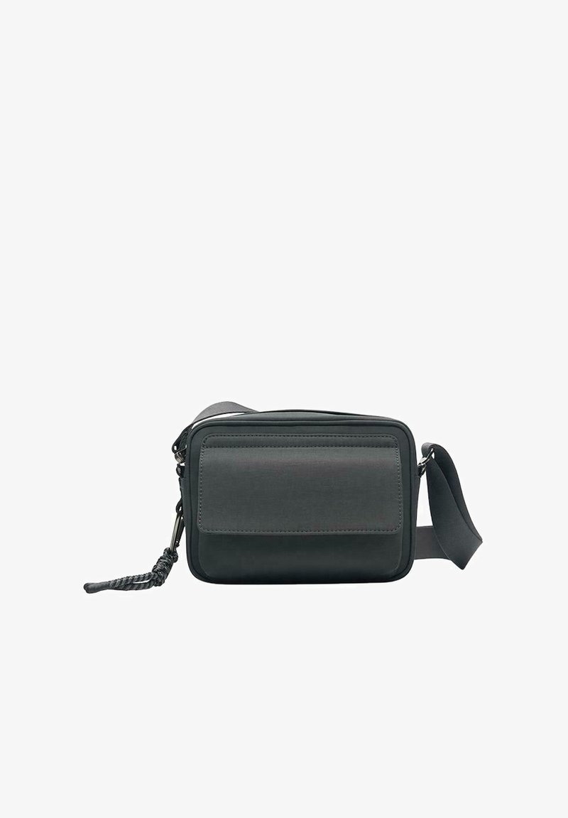 Petit sac bandoulière noir avec une poche à rabat sur le devant, fermeture éclair, sangle réglable et détail de pompon tressé sur le curseur de la fermeture.