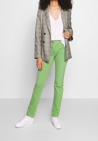 Graham kariertes Blazer mit doppelten Knöpfen, kombiniert mit grünen Hosen und weißen Turnschuhen. Das Outfit verbindet strukturierte und lässige Elemente.