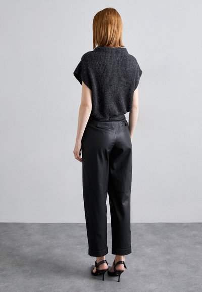 Κοντομάνικος, σκούρος γκρι πλεκτός τοπ συνδυασμένος με ψηλόμεσα μαύρα δερμάτινα παντελόνια. Διαθέτει διπλωμένο στρίφωμα και εφαρμοστή σ silouette, συμπληρωμένο από μαύρες σανδάλες.