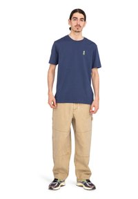 Navy blue cotton t-shirt with a small green logo on the chest, paired with light khaki cargo pants and multi-colored sneakers.