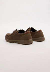 Zapatos de cuero marrón con una textura suave, bajo perfil y acentos en marrón oscuro contrastante. Presentan detalles de costura y una suela de goma duradera.