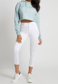 Felpa cropped azzurro chiaro con coulisse, abbinata a jeans skinny bianchi e sneakers bianche. Tessuto liscio con una silhouette aderente.