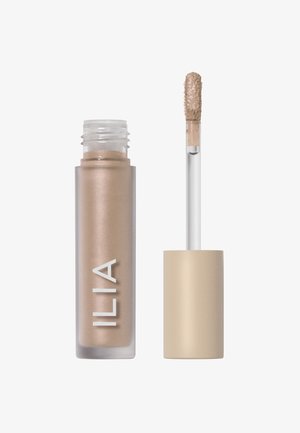 ILIA flydende highlighter i et klart glasrør med en frostet guldfinish, har en doughtapplikator og en lys beige nuance med glitrende effekt.