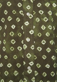 Skjorta med krage i mörkgrön tyg, med ett diamantmönster i ljusgrönt. Fem knappar framtill, slät yta.