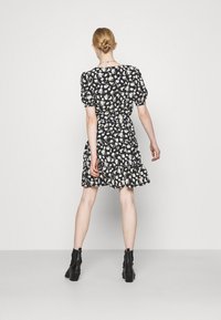 Robe noire à motifs floraux avec manches bouffantes, taille cintrée et jupe évasée. Le tissu présente un motif texturé avec des fleurs jaunes et blanches.