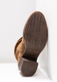 Bruna mockaläders ankelskor med en texturerad gummisula med ett vävt mönster, accentuerade av en slät läderklack och minimalistisk design.