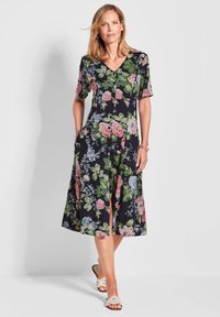 Robe à imprimé floral bleu marine avec des manches courtes, un décolleté en V, deux poches latérales et une fente à l'avant. Fabriquée en tissu léger et respirant.