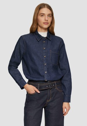 Dark denim shirt with long sleeves, button front, pointed collar, single chest pocket, orange stitching, paired with dark denim pants.
