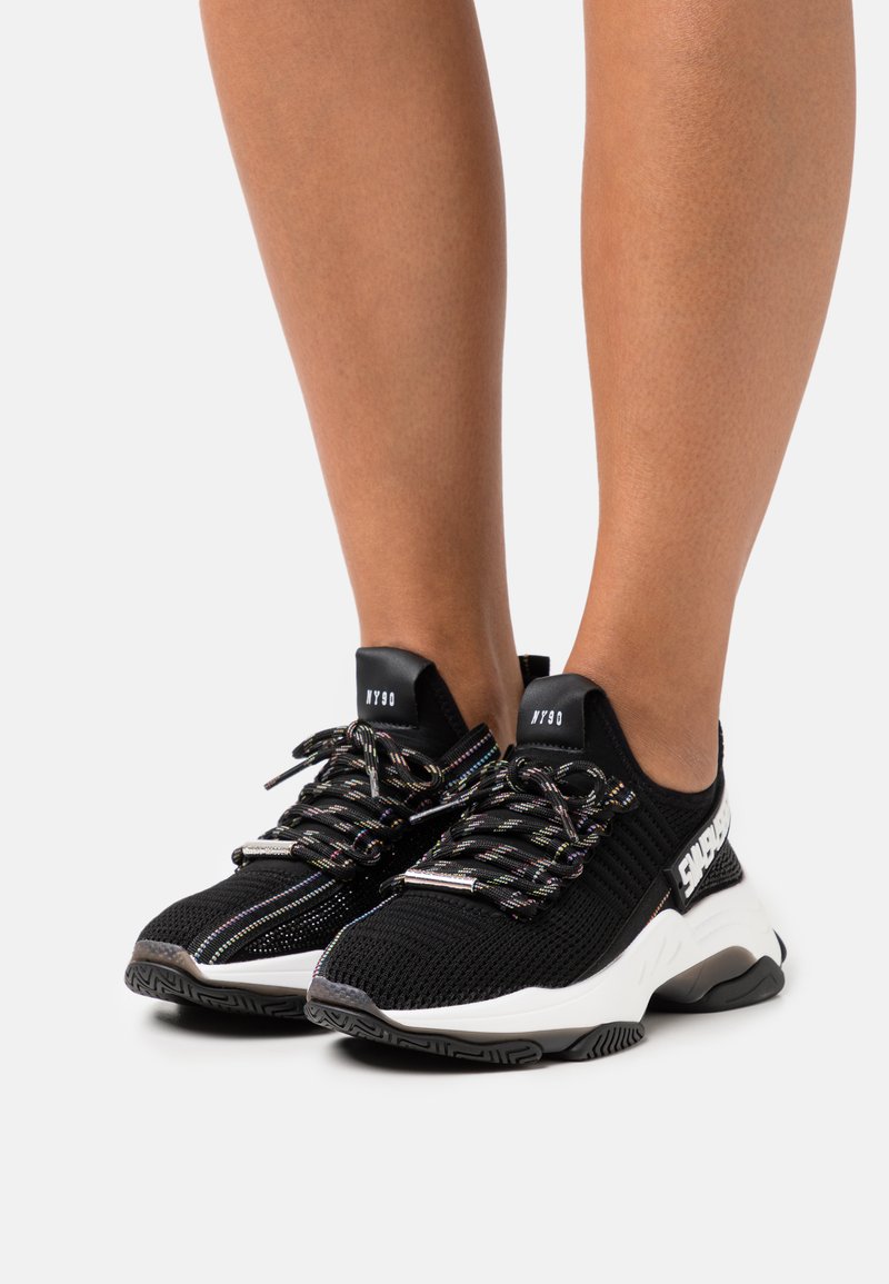 Scarpe da ginnastica nere in rete con dettagli riflettenti, dotate di una suola bianca imbottita e lacci multicolori. Branding sul lato.
