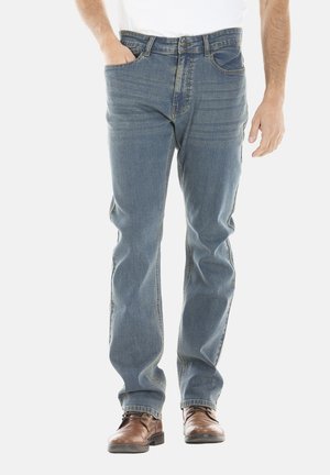 Jean en denim bleu avec une coupe droite, comportant cinq poches, une fermeture éclair et un léger délavage à l'avant. Associé à des chaussures en cuir marron.