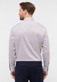 Camicia chiara a motivo con un piccolo design geometrico, polsini a bottone e colletto classico, abbinata a pantaloni scuri.