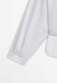 Manche blanche longue avec poignet, faisant partie d’un vêtement taillé sur mesure, présenté sur un fond blanc uni.