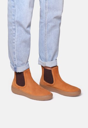 Bottes chelsea en cuir tan avec des panneaux élastiques sur les côtés, des accents marron et des semelles en caoutchouc texturé, assorties à un jean bleu clair retroussé.