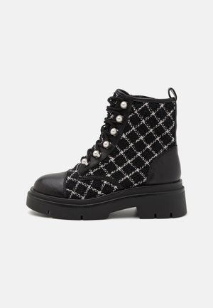 Bottine noire avec motif croisé blanc, crochets à lacets en perles, semelle épaisse, bout en cuir et languette arrière.