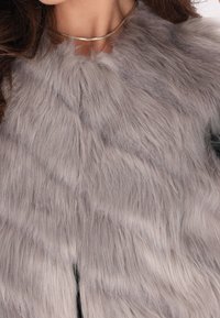 Faux-Fur-Weste in Hellgrau mit einer weichen Textur und diagonalen Mustern. Verfügt über einen runden Halsausschnitt und ist über einem schwarzen Kleidungsstück geschichtet.