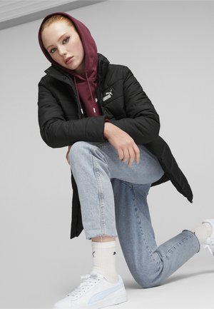 Chaqueta acolchada negra con capucha, sudadera burdeos debajo, jeans de mezclilla azul claro y zapatillas blancas con detalles azules. Diseño simple, minimalista en la marca.