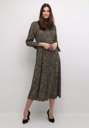 Langärmliges, knöpfbares Kleid mit schwarz-beigem Muster. Verfügt über einen Gurtbündchen in der Taille und einen fließenden, knielangen Rock.