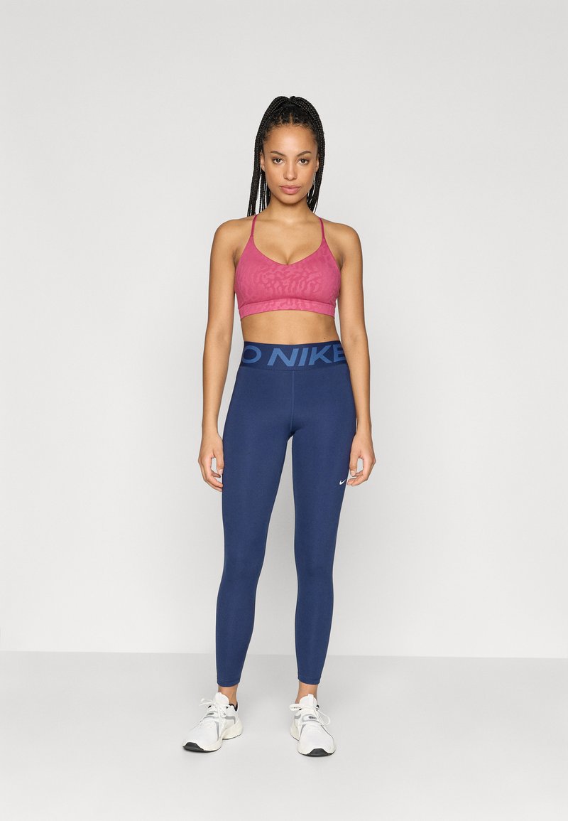 Pink sports bra with a textured pattern, paired with navy leggings featuring a bold "NIKE" logo on the waistband, completed with white sneakers.