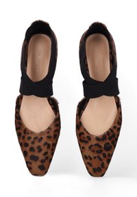 Een paar ballet flats met panterprint, zwarte elastische kruislussen en beigekleurige zolen op een witte achtergrond.