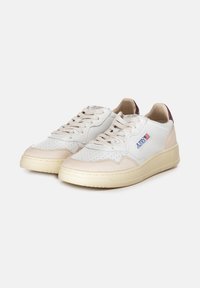 Sneakers in pelle bianca con accenti beige, punta perforata, lacci piatti e suola in gomma beige texturizzata. Presenta un piccolo logo applicato.