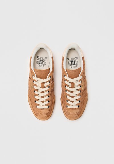 Sneaker in suede marrone con lacci beige, design perforato, logo inciso di lato e dettagli testurizzati. Interno bianco e suola piatta.