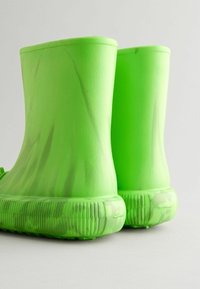 Bottes en caoutchouc vertes avec une texture lisse, des bords arrondis et des semelles striées. Semi-transparentes avec un motif marbré.