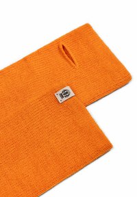 Knitted orange fabric with a textured finish, featuring a cutout hole and a branded label stitched at the edge.