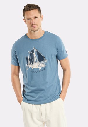 T-shirt en coton bleu avec un graphique de poisson blanc et de voilier accompagné de texte. Manches courtes et col rond, coupe décontractée. Tissu texturé.
