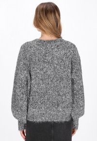 Grå stickad tröja med lös passform, texturerat tyg och vida ärmar. Sänkningen är något kortad, vilket ger en fluffig uppenbarelse.