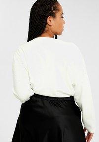 Vit långärmad tröja med dekorationer på axlarna, i kombination med en svart satin kjol. Mjuk textur och avslappnad passform.