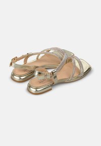 Sandales métalliques dorées avec des talons blocs plats, présentant des brides entrecroisées ornées de strass scintillants et une fermeture à boucle.