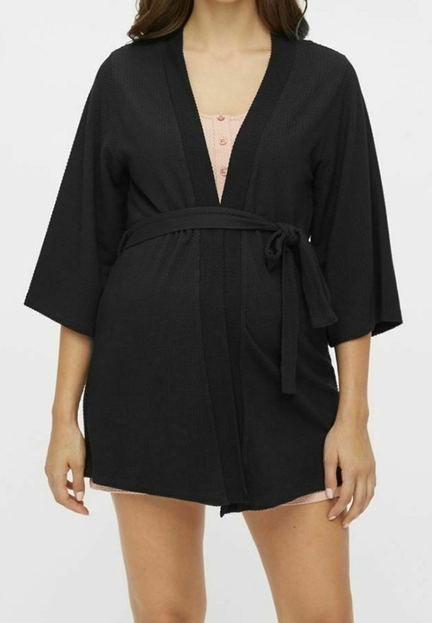 Svart texturerad robe med breda ärmar, ett bälte i midjan och V-ringning, lager på lager över ett ljust rosa plagg med knappar.