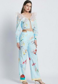 Two-piece outfit featuring a cropped, light blue jacket with ruffled transparent collar and matching wide-leg pants decorated with colorful patterns.