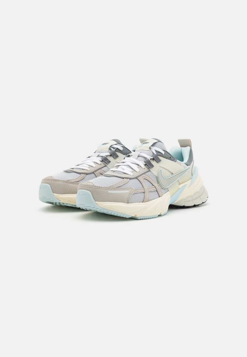 Zapatillas con una parte superior de malla gris claro, acentos de cuero beige y detalles en azul. Presentan cordones blancos y una suela texturizada.