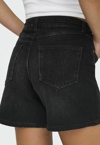 Shorts en denim noir à taille haute, dotés de deux poches arrière, d'un ourlet propre et d'une texture légèrement délavée. Aucun détail de quincaillerie visible.