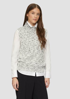 Knitted sleeveless sweater in white with gray speckles, paired with a white collared shirt. Soft texture, casual fit, and no visible hardware.