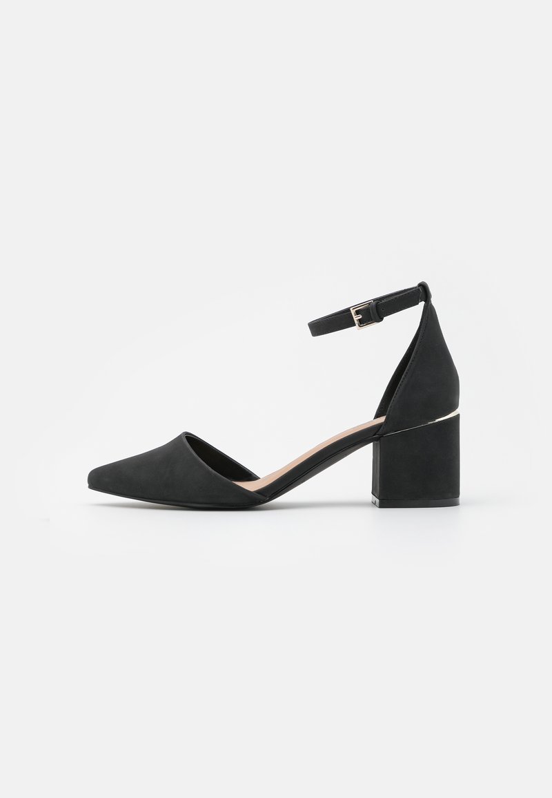 Chaussure noire pour femme à talon moyen, bout pointu, bride de cheville avec boucle et talon épais, sur fond blanc uni.
