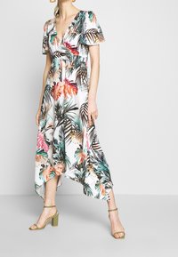 Blommig midiklänning i lätt tyg, med djup V-ringning, puffärmar och ojämn fåll. Färgglatt tropiskt mönster i grönt, rosa och orange.