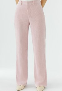Pantalon large en velours côtelé rose avec nervures verticales, doté d'une taille ajustée et de poches latérales. Surface texturée pour un intérêt visuel.