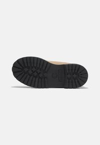 Sole in suede marrone con una resistente suola in gomma nera caratterizzata da scanalature profonde e un logo per garantire trazione e durata.