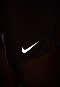 Mustat urheilushortsit, jotka on valmistettu sileästä kankaasta ja joissa on selkeä valkoinen Nike-logo oikeassa alareunassa. Yksinkertainen muotoilu ilman näkyviä kuvioita.