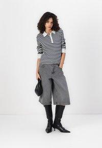 Striped langermet polo skjorte i marineblå og hvit, sammen med beskårne grå denimbukser. Avsluttet med svarte spisse støvler og en svart håndveske.
