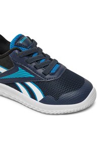 Tyrkysovo-modrá a biela športová obuv s čiernymi šnúrkami, modrou sieťovanou jazykovou časťou, textúrovaným prstom a bielou podrážkou v detailnom pohľade.