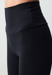 Leggings neri a vita alta realizzati con un tessuto elastico e morbido. Presentano una cintura ampia senza motivi o dettagli distintivi.