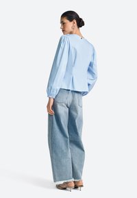 Light blue blouse with gathered long sleeves, a back pleat, and a button closure. Paired with oversized light denim jeans and heels.