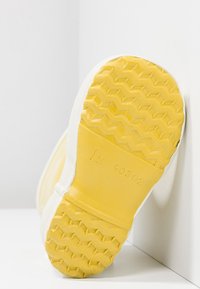 Geel rubberen zool met een gestructureerd oppervlak, met een zigzagpatroon. Witte bovenrand met zichtbare naaddetails.