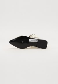 Pointed-toe high heel shoe featuring a white textured upper with silver hardware and a black flat heel with a ribbed pattern.