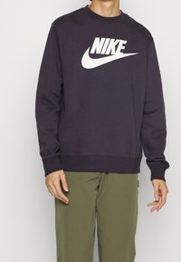 Purple Nike sweatshirt with white logo, crew neck, long sleeves, ribbed cuffs, and hem. Worn over olive green pants.