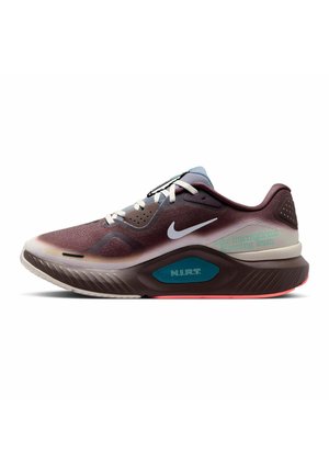Dunkellila Nike Laufschuh mit weißem Swoosh, weißen Schnürsenkeln, dicker gepolsterter Sohle und türkisfarbenem Detail mit der Aufschrift N.I.R.T. an der Seite.